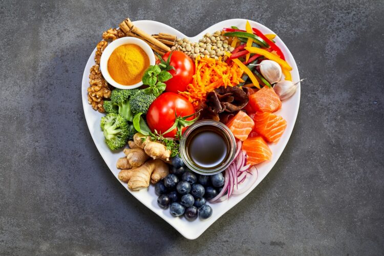 Healthy diet for the cardiovascular system with a heart-shaped plate of acai, lentils, soy sauce, ginger, salmon, carrot, tomato, turmeric, cinnamon, walnuts, garlic, peppers, broccoli, basil, onion