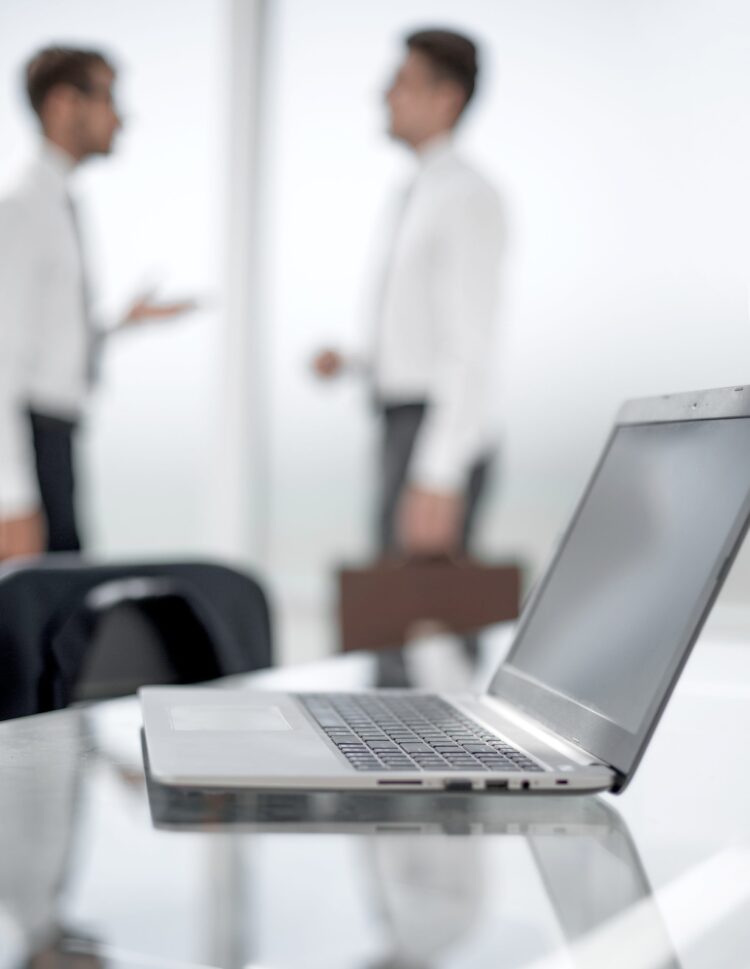 Focus on laptop on the table. Blurred people on background